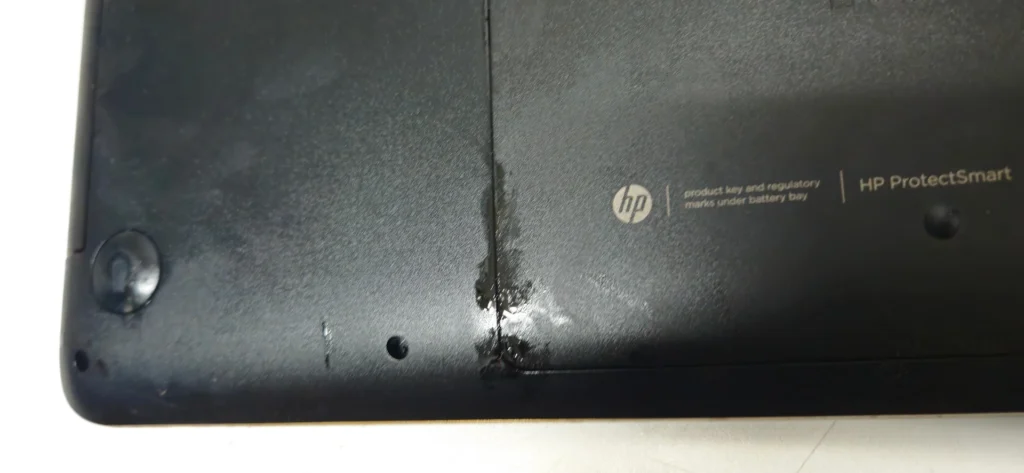 Detailansicht einer beschädigten und verschmutzten Stelle an der Notebook-Unterseite